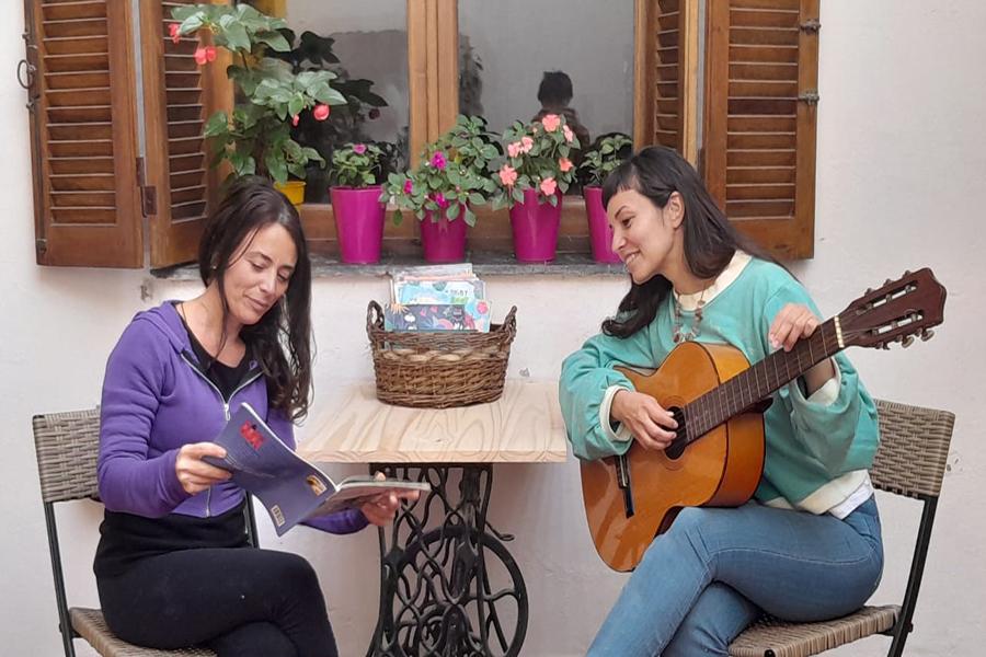 Foto de dos mujeres. Una tocando la guitarra y otra leyendo un libro.