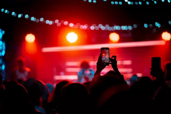 Escenario musical iluminado por luces rojas y celulares filmando la escena