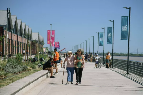 personas caminando por la costanera, paseo ribereño entre los galpones y el río paraná
