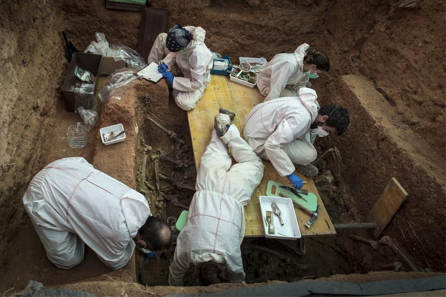 excavación arqueológica de una fosa común con restos óseos y un equipo de forenses trabajando