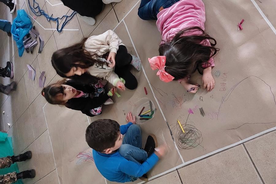 Niños y niñas recostados en el suelo dibujando sobre hojas de papel.