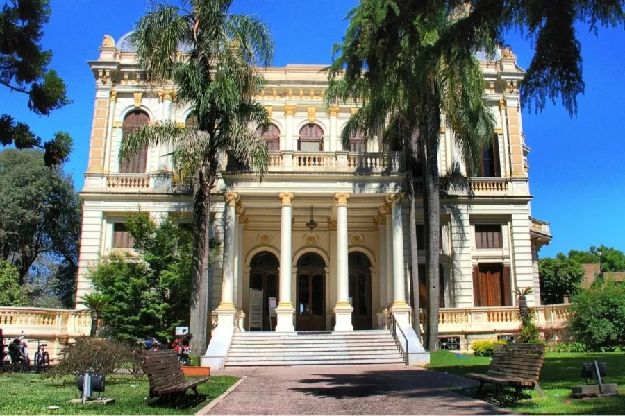 Imagen del edificio de villa hortensia, antigua casona de dos pisos, con puertas muy grandes, balcones y ventanales. Dos palmeras en el frente del jardìn