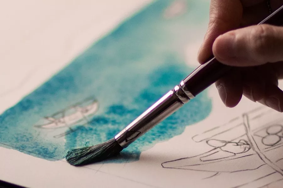 Es la imagen de una mano sosteniendo un pincel y pintando un dibujo