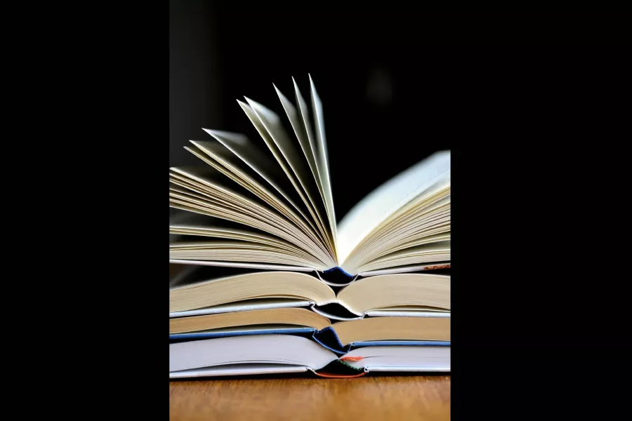 Se observan cuatro libros abiertos, uno arriba del otro, sobre un mueble.