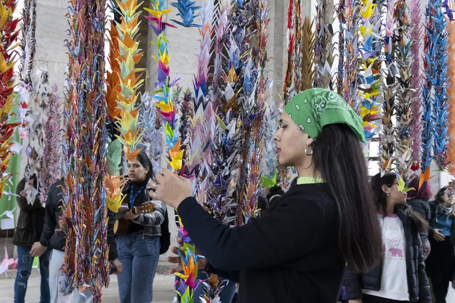 Muchas tiras de grullas de papeles de colores colgadas y hay una chica tocando una de ellas con sus manos