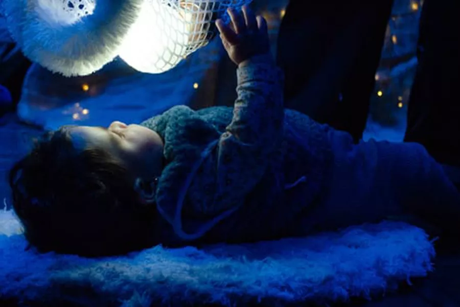 es la imagen de un bébe acostado en un almohadón y observando un objeto con luces
