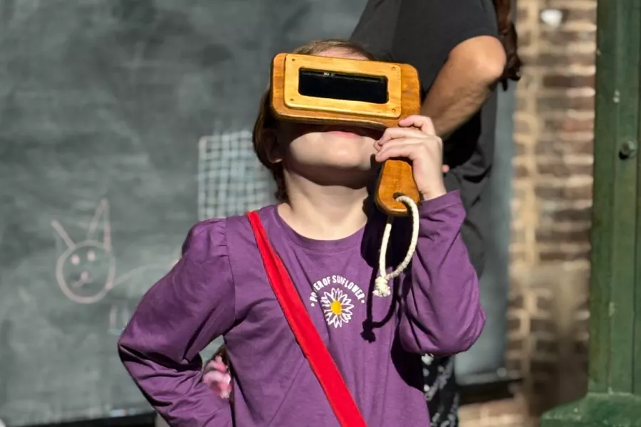 Niña mirando el cielo con un visor para ver el sol