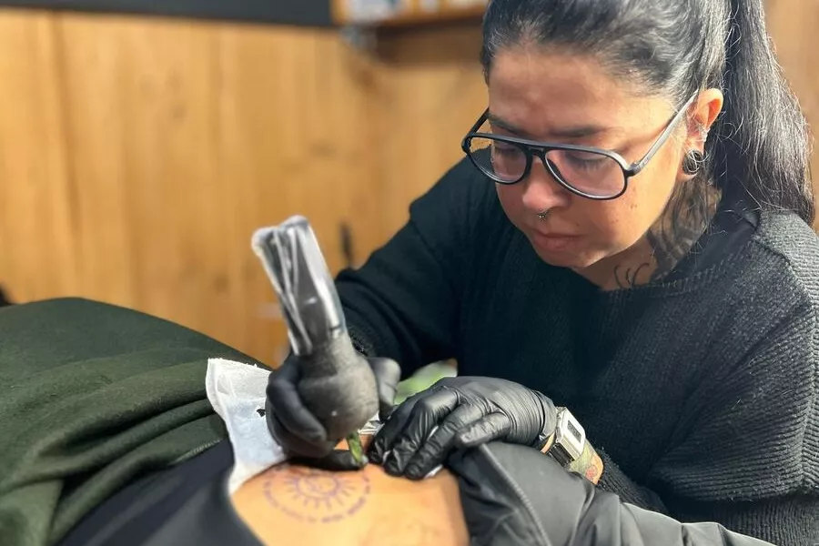 Es la imagen de una tatuadora tatuándole la espalda a una chica