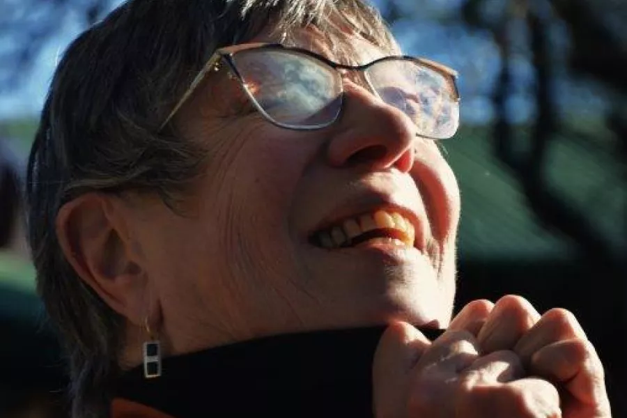 Fotografía de una mujer de pelo corto y anteojos, sonriendo, que mira hacia arriba y el sol da en su cara.