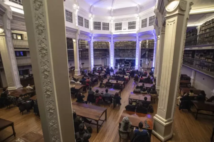 Es la imagen de una de las salas de la Bibilioteca Argentina; es un espacio amplio de techo alto, donde hay mesas para disfrutar de la lectura y charlas. 