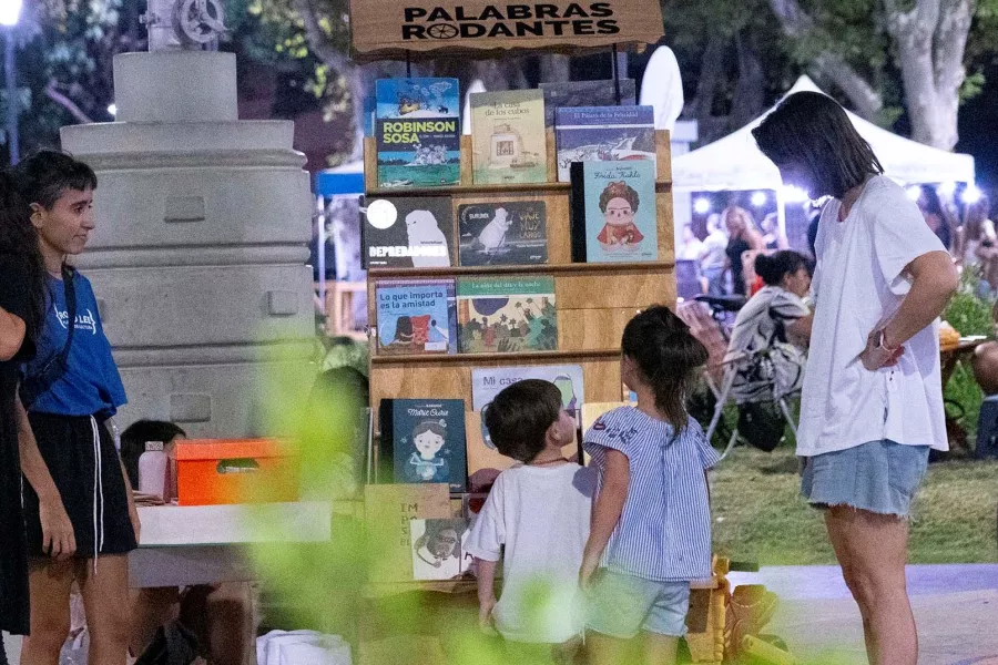 una biblioteca móvil en una plaza. Hay dos mujeres adultas y un niño y una niña, mirando los libros.