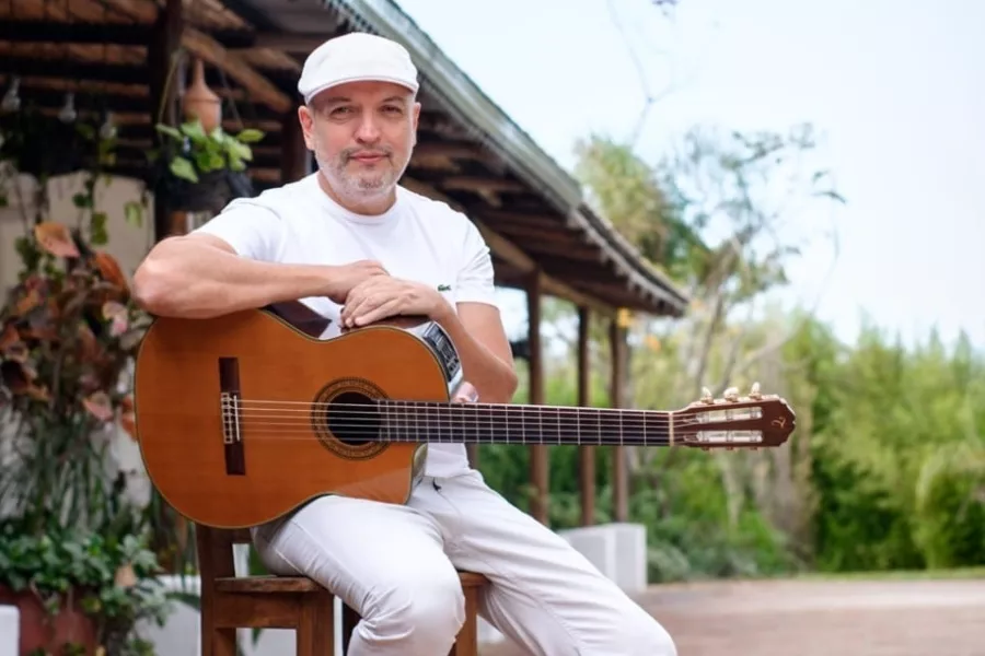 Es la imagen de un músico posando para una foto, está sentado y con su guitarra