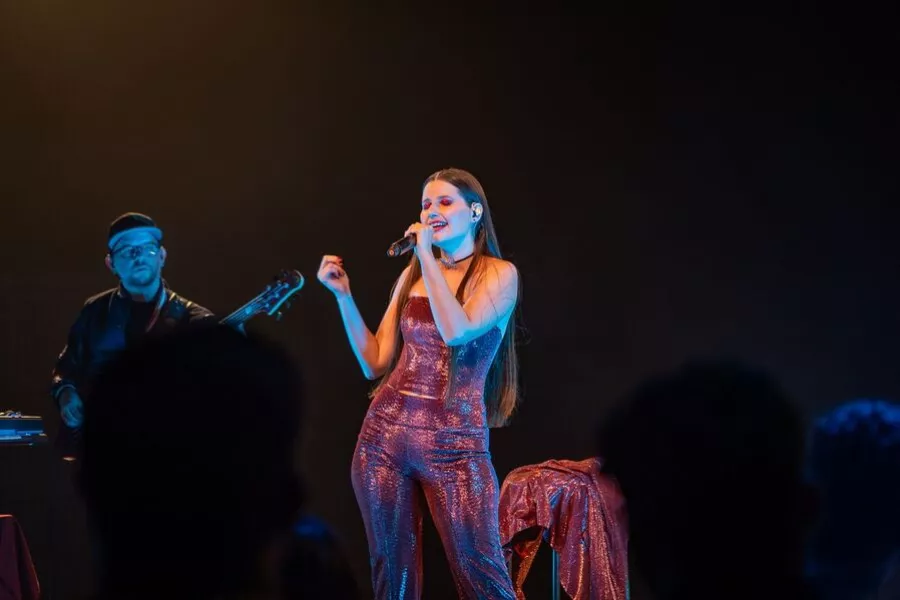 Es la imagen de una cantante en un escenario, junto con una persona tocando la guitarra