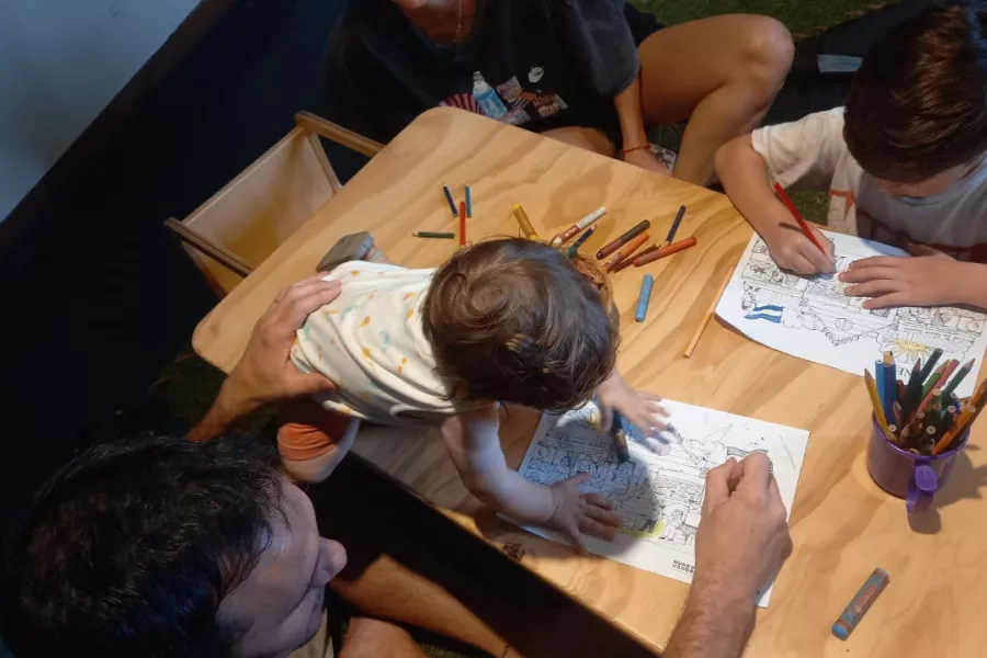 Dos niños dibujan y pintan junto a su papá. La imagen está tomada de manera cenital, desde arriba, en una de las salas del Museo de la Ciudad.