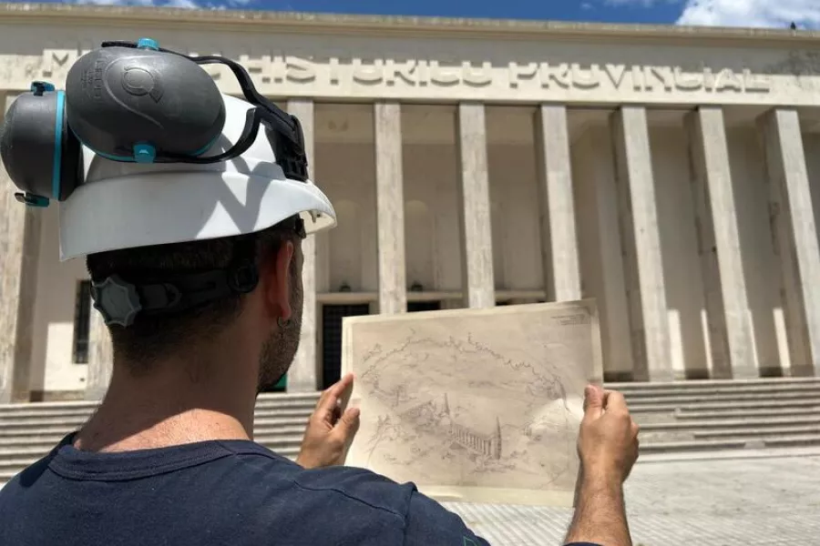 Es la imagen de un obrero sosteniendo un diseño antiguo del edificio y de fondo el museo en la actualidad