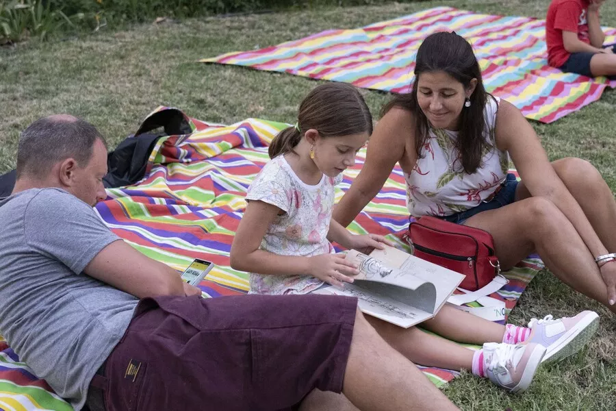 Es la imagen de una familia leyendo un libro en un parque 