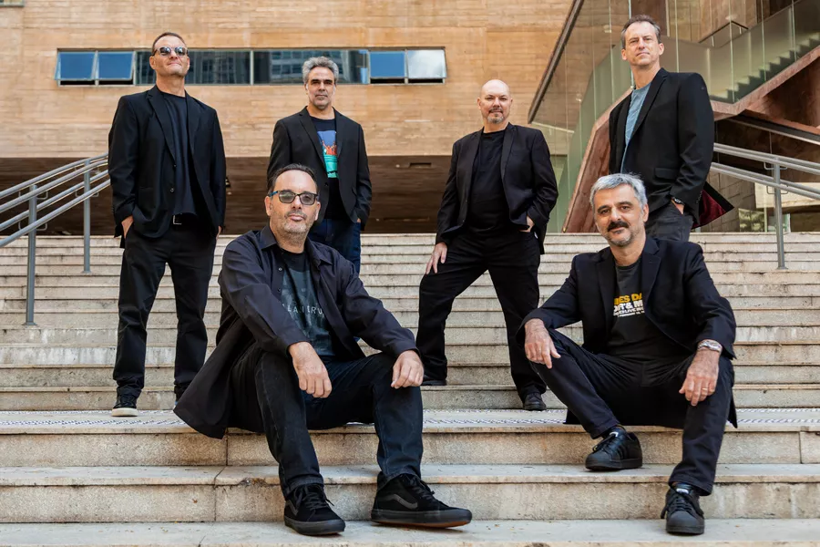 Es la imagen de 6 músicos posando para una fotografía en una escalera: 2 sentadas y 4 paradas