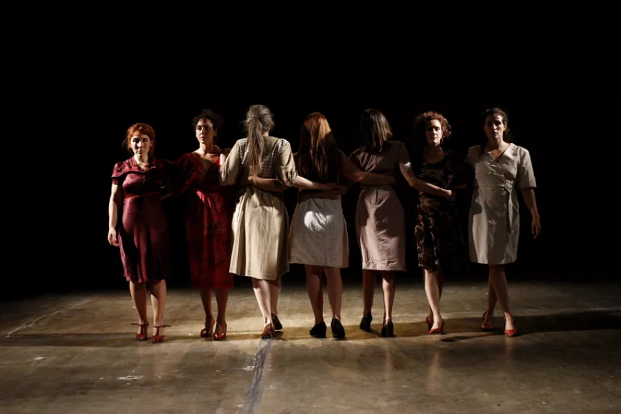 Es la imagen de siete actrices realizando una escena. Están paradas y algunas están mirando a la cámara y otras de espalda