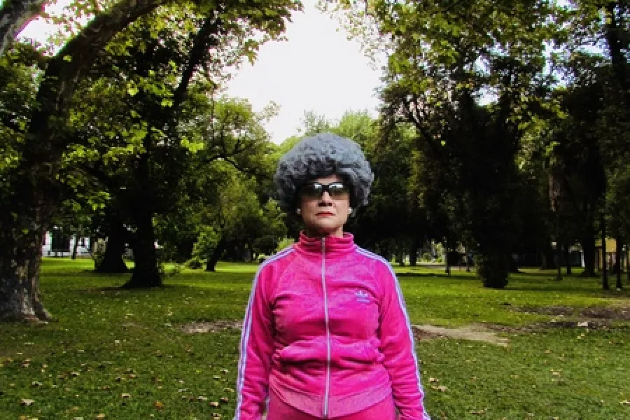 Es la imagen de una actriz caracterizada por su personaje: ropa deportiva rosa, lentes de sol y una peluca gris
