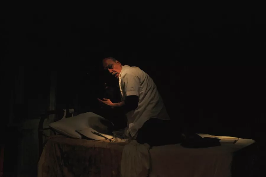 Es la imagen de un actor caracterizado como su personaje, que está sentado en una cama y mirando a un punto fijo