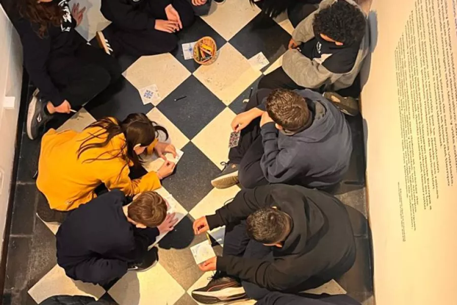 Un grupo de escolares dispuesto en ronda arman distintos diseños de azulejos, la imagen está tomada desde arriba a vuelo de pájaro en el interior del museo. 