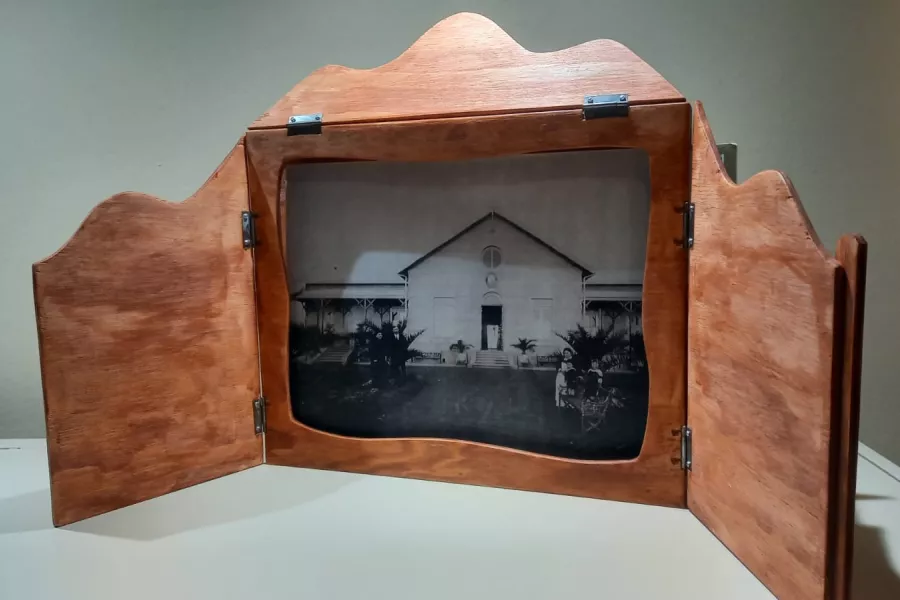 En primer plano apoyado sobre una superficie clara un teatrillo de madera, clásica forma de presentar esta forma de teatro originaria de Japón, completamente abierot muestra una imagen antigua del edificio del Museo de la Ciudad.