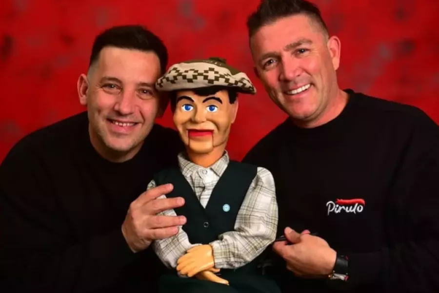 Es la imagen de dos personas sonriendo. En el medio hay una marioneta que se llama Pirulo