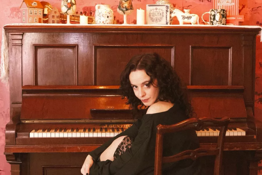 Es la imagen de una cantante argentina sentada en un piano y mirando a la cámara