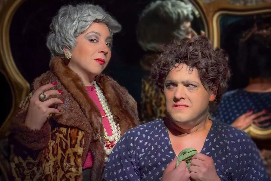 Es la imagen de dos personajes de una obra de teatro. Tienen pelucas y ropa de señora grande