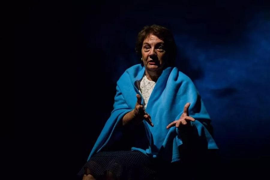 Es la imagen de una actriz caracterizada como su personaje: tiene un poncho azul en un fondo negro con una cortina de humo