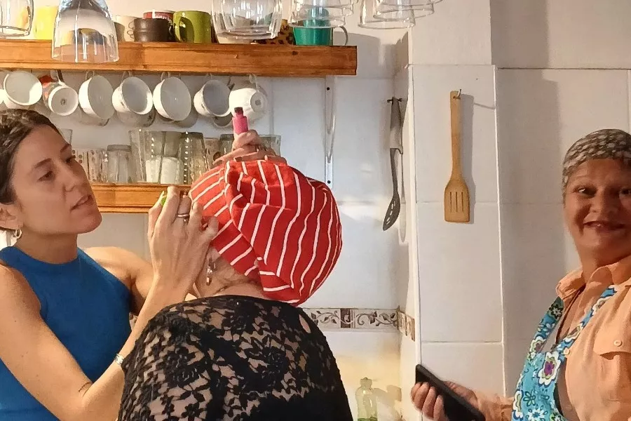Es la imagen de una actriz siendo maquillada mientras su compañera de escena mira a cámara y sonrie 