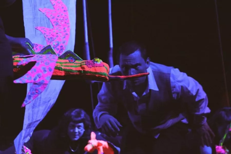 Es la imagen de un actor y una actriz observando expectantes a un títere con forma de serpiente