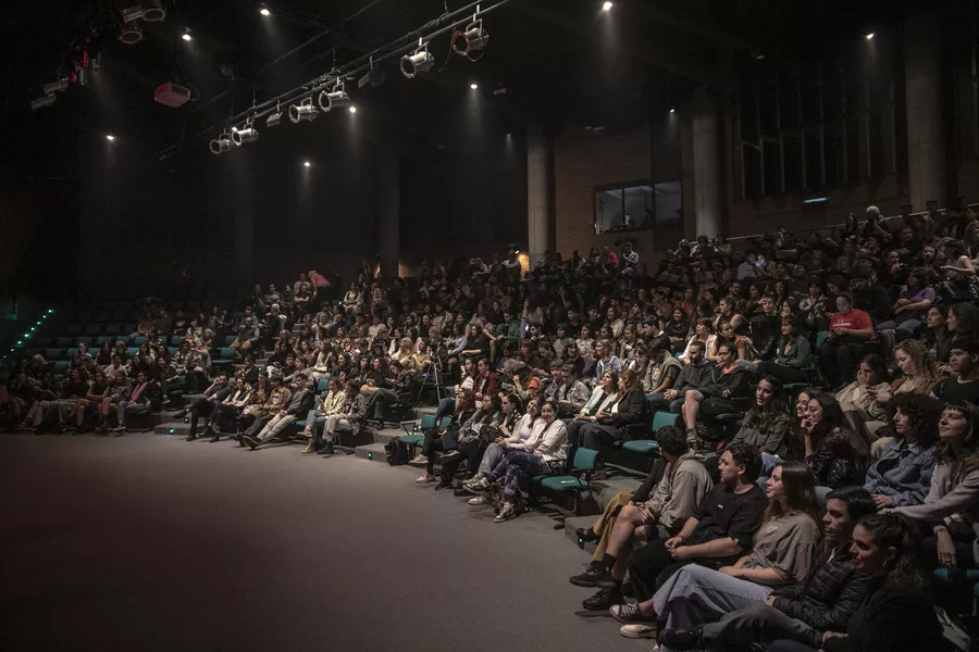 Es la imagen del interior de la sala de un teatro, en la misma hay tribunas y personas sentadas esperando a que comience la obra