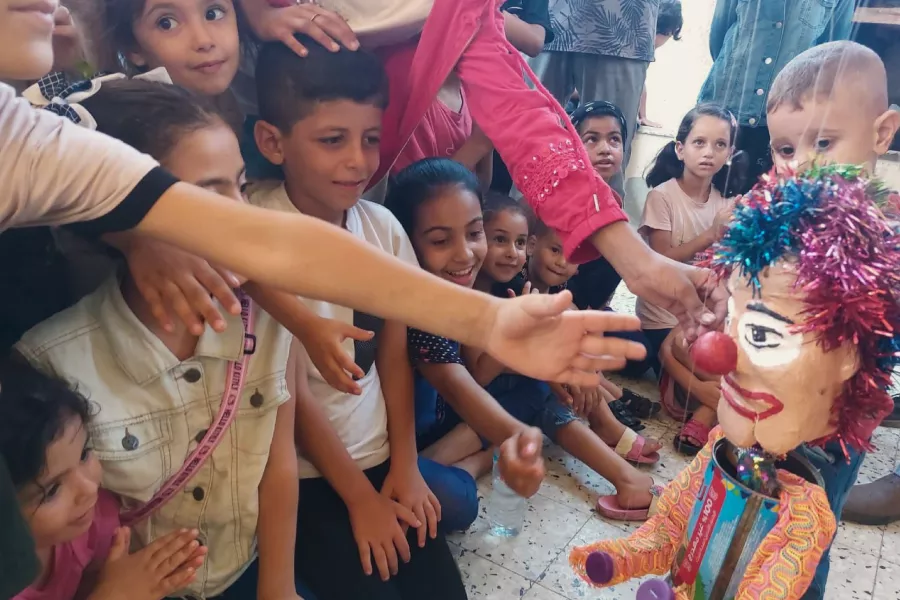 Niñas y niños extendiendo sus brazos a la marioneta RITAL, la piloto.