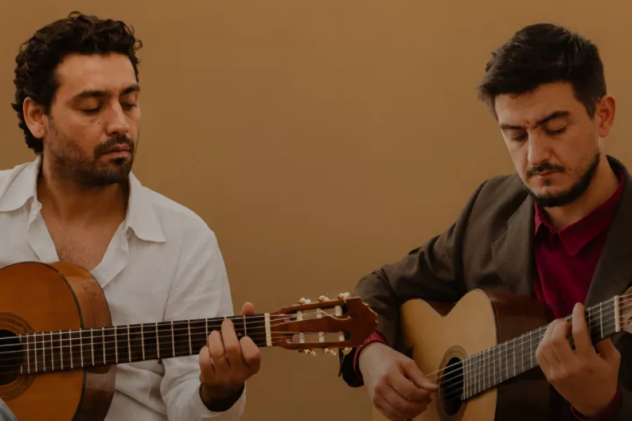 Es la imagen de dos músicos tocando la guitarra