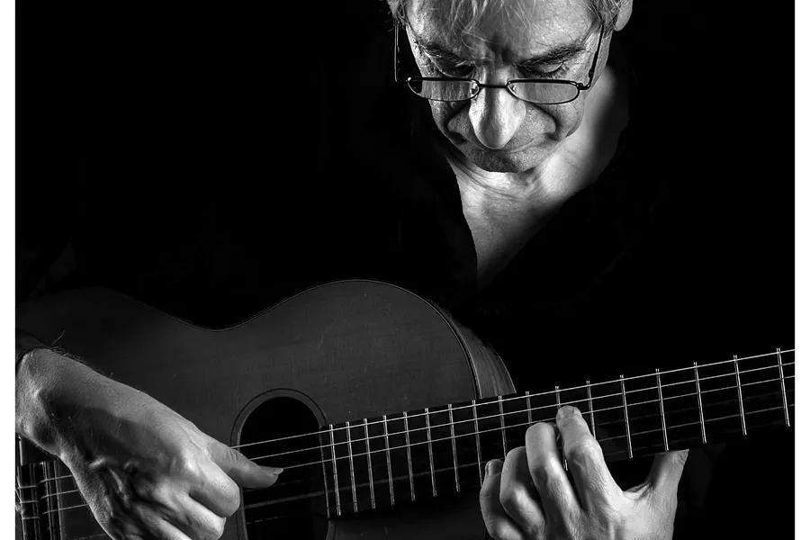 Es la imagen de un músico tocando la guitarra. La foto está sacada en blanco y negro