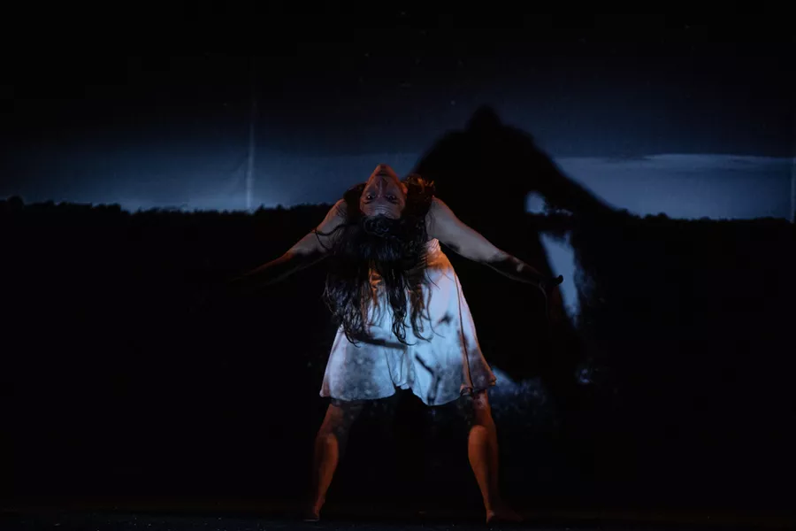 Es la imagen de una bailarina realizando una coreografía. Está de espalda al escenario y mirando a él