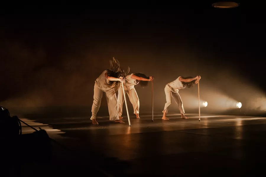 Es una imagen de un grupo de bailarinas realizando una coreografía. Tienen vestimenta blanca y palos 