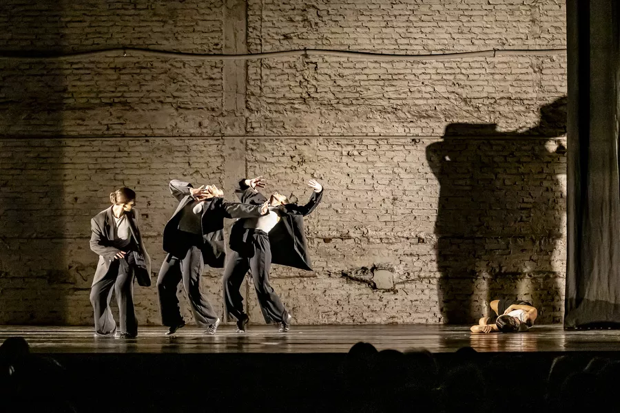Es la imagen de un grupo de bailarines que están haciendo una coreografía. Están vestidos de traje